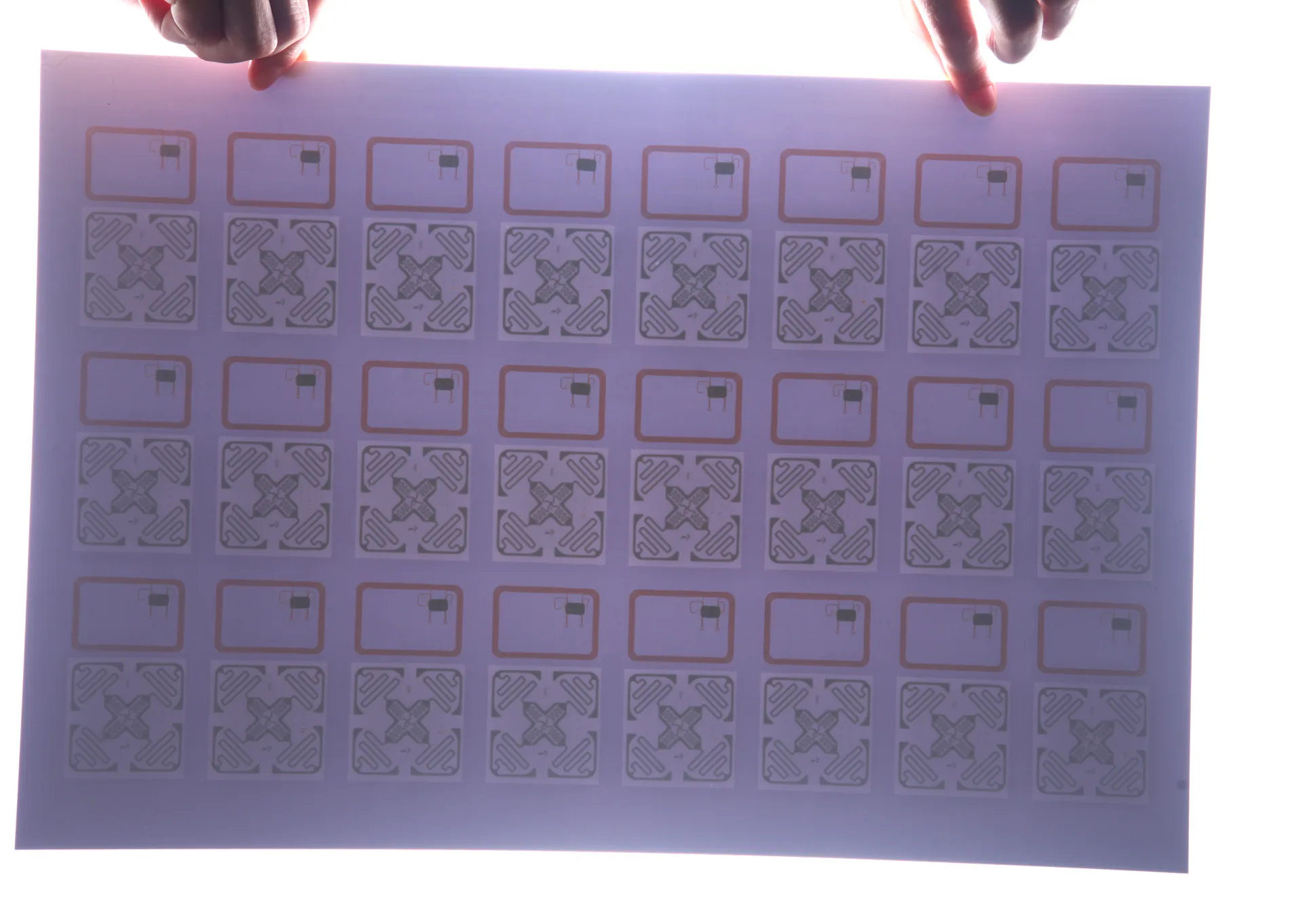 Backlit RFID card inlay sheet showing etched HF and UHF antenna arrays, by RFIDAK Shenzhen prelam factory