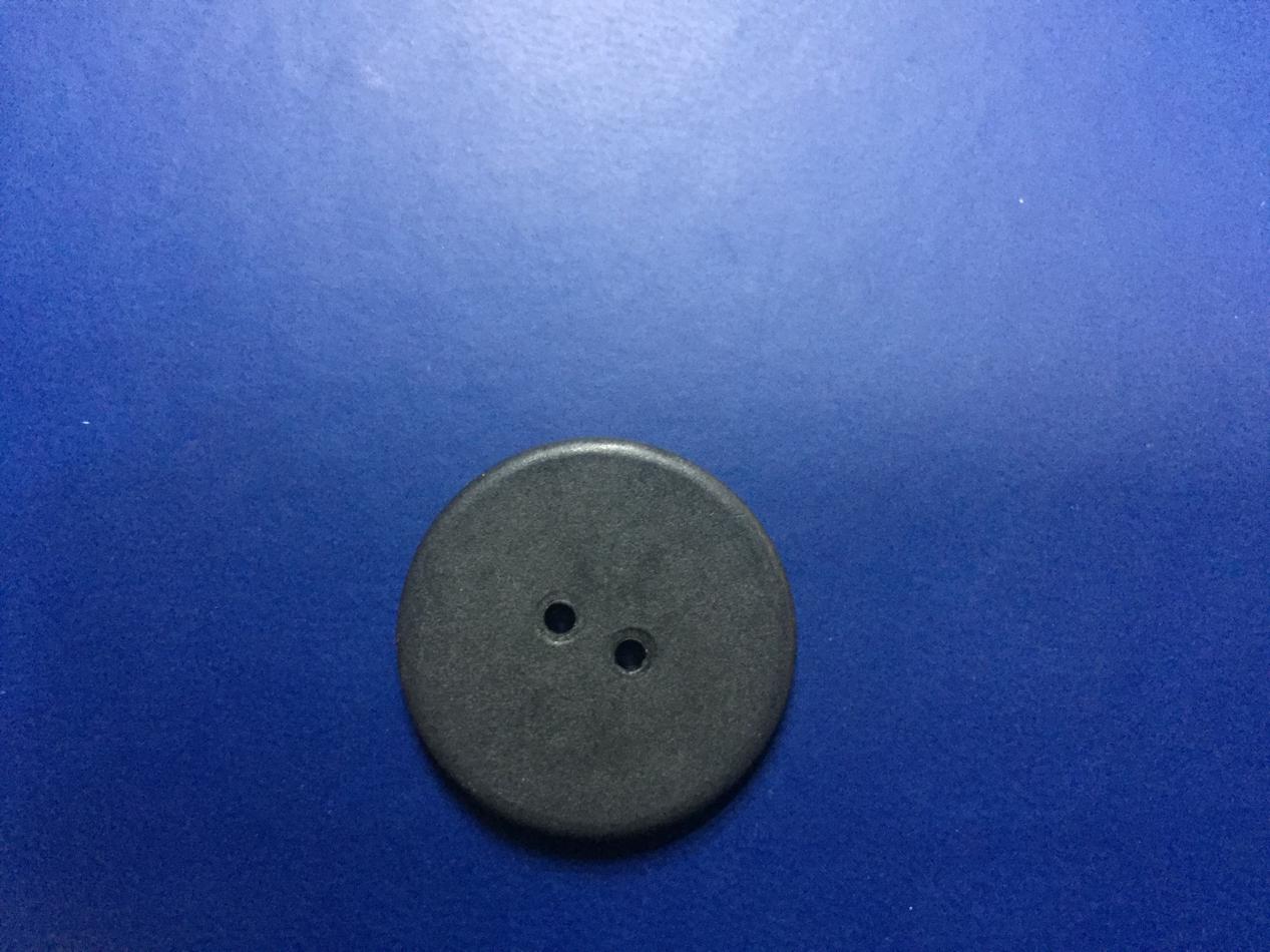 Black round laundry button with two sewing holes on a blue background.